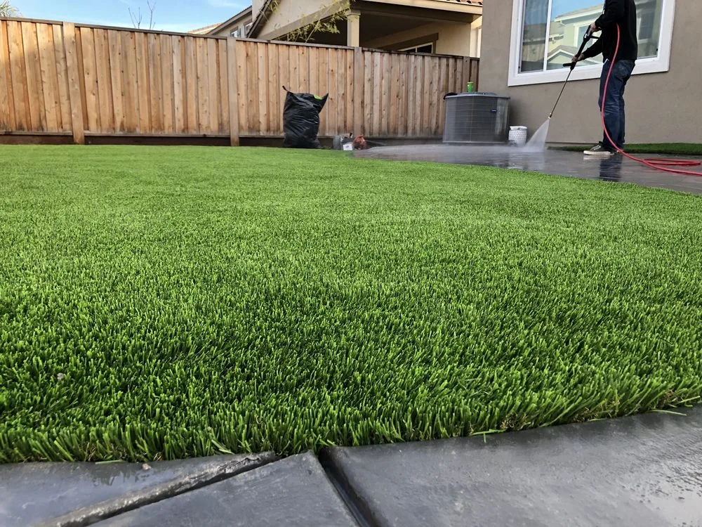 Technician pressure-washing newly installed artificial turf