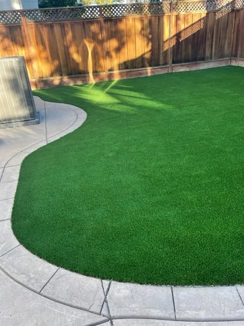 Curved backyard artificial turf installation along a fence line