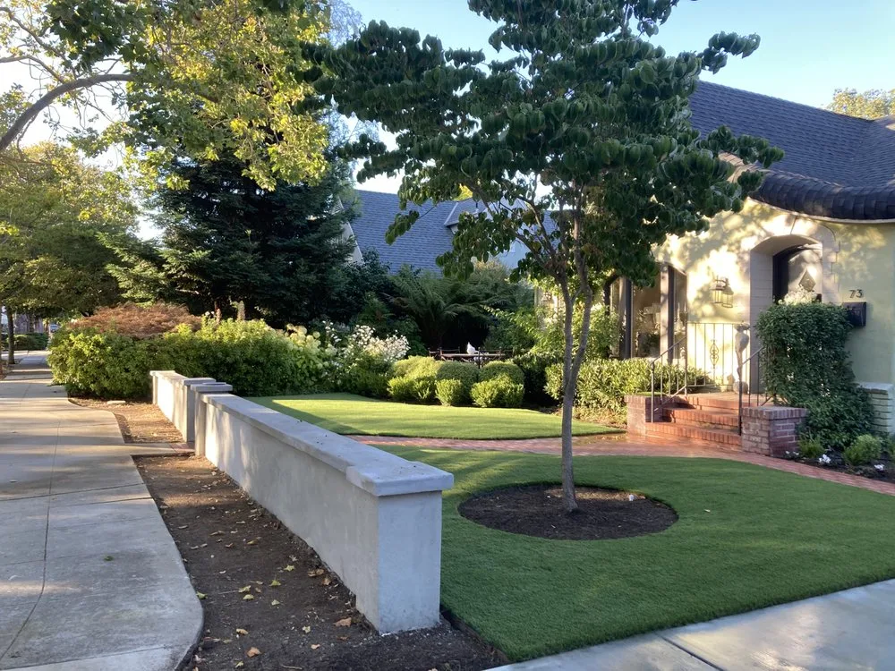Upscale front yard artificial turf installation with stone wall